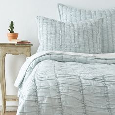 a bed with blue comforter and pillows on it next to a small potted plant