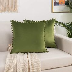 two green pillows sitting on top of a white couch next to a potted plant