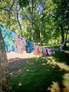 clothes hanging on a line in the park with trees and grass behind them, all covered by colorful tie - dyes