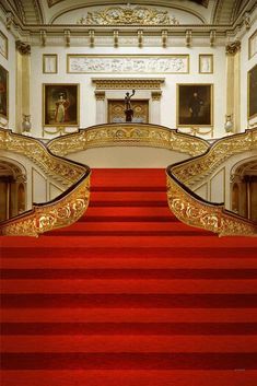 a red carpeted staircase leading up to a white building with paintings on the walls