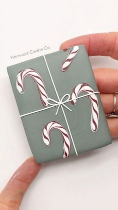 a hand holding a green and white square ornament with candy canes on it