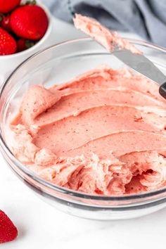 a bowl filled with pink frosting next to strawberries