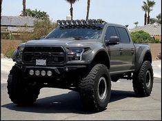 a large truck with big tires parked in a parking lot next to some palm trees