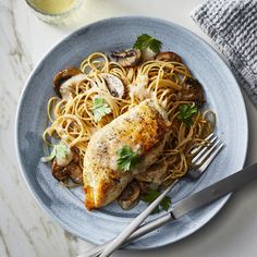 a blue plate topped with chicken and noodles next to a glass of orange juice on top of a white table