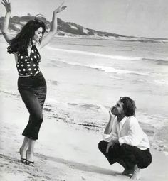 a man kneeling down next to a woman on a beach