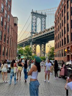 many people are walking on the sidewalk near some buildings and a bridge in the background