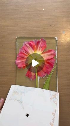 a person holding up a flower in front of a wooden table with a video screen