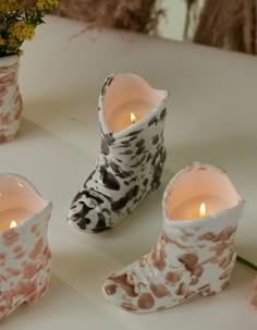 three white and brown vases with candles in them sitting on a table next to flowers