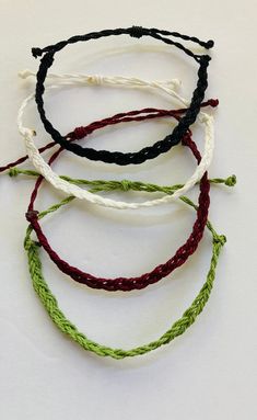 four different colored bracelets on a white surface, one with green and red thread