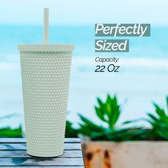 a white cup sitting on top of a wooden table next to a plant and ocean