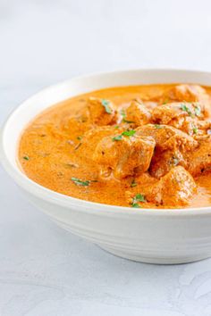 a white bowl filled with meat and sauce on top of a table next to a spoon