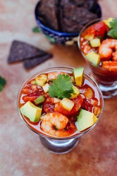 two glasses filled with food and garnished with cilantro, avocado, and shrimp