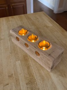 three lit candles in a wooden holder on a table