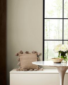 a vase with flowers sitting on top of a white table next to a large window