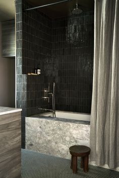 a black and white tiled bathroom with a stool next to the bathtub, shower curtain, and window