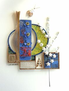 a blue and yellow plate sitting on top of a white wall next to a vase with flowers