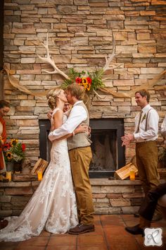 a bride and groom kissing in front of a stone fireplace with antlers on it