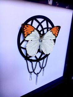 an orange and white butterfly sitting on top of a black circular object with chains hanging from it's sides