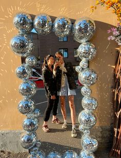 two women are taking a selfie in front of a mirror ball sculpture on the sidewalk