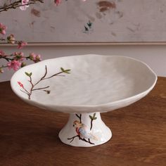 a white bowl sitting on top of a wooden table next to a vase with pink flowers