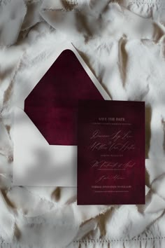 an elegant burgundy and white wedding suite is displayed on a bed sheet with the word save the date printed on it