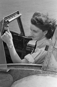 a woman sitting in the driver's seat of an old fashioned car, looking at her phone