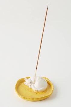 a white cat figurine sitting on top of a yellow plate with a stick sticking out of it