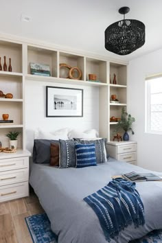 a bed sitting in a bedroom under a chandelier next to a shelf filled with vases