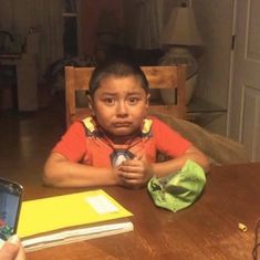 a young boy sitting at a table with an open cell phone in front of him