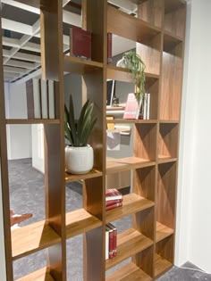 a wooden book shelf with books and plants on it in an empty room next to a carpeted floor