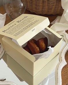 two pastries in a box sitting on a table next to a basket and napkins