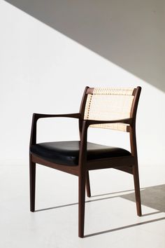 a wooden chair with black leather seat and armrests in front of a white wall