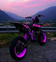 a pink and black dirt bike parked on the side of a road at dusk with mountains in the background