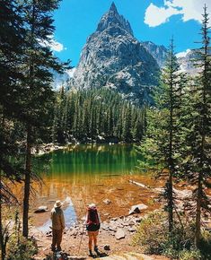 two people are standing at the edge of a mountain lake