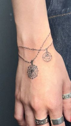 a woman's hand with three different tattoos on her wrist and two rings around the wrist