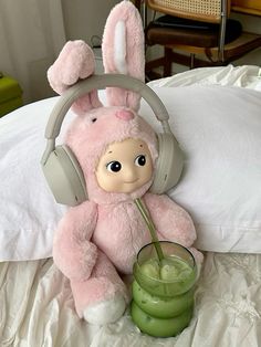 a pink stuffed animal with headphones on sitting on a bed next to a green drink