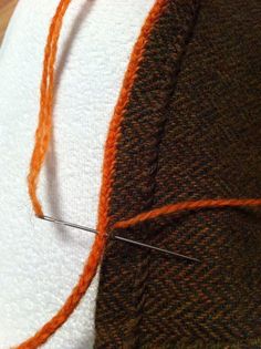 an orange thread is hooked up to the side of a white piece of cloth with scissors in it