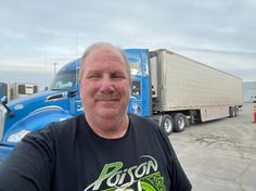 a man is standing in front of two semi - trucks, one blue and the other white