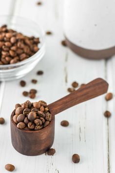 a wooden spoon filled with coffee beans on top of a white table next to a cup