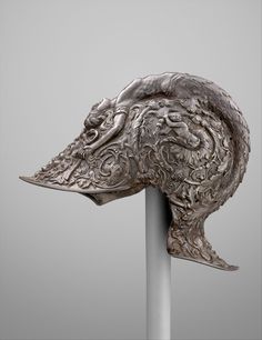 an intricately carved metal animal head on a silver pole in front of a gray background