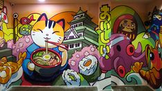 a colorful wall painted with cats and other animals eating out of bowls in front of it