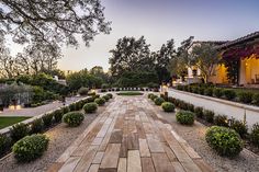 an outdoor walkway leading to a house with trees in the back ground and bushes on either side