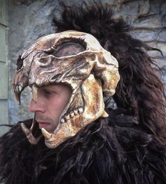 a man wearing an animal mask in front of a stone wall