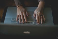 a person typing on a laptop keyboard with their hands resting on the top of the keyboard