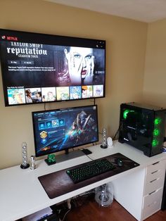 a computer desk with two monitors, keyboard and mouse on it in front of a flat screen tv