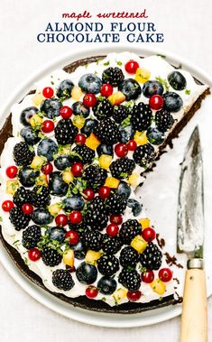 a white plate topped with a cake covered in berries and blackberries next to a knife