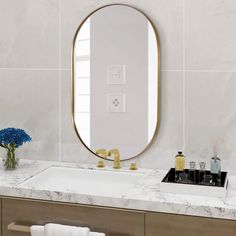 a bathroom with marble counter tops and a large round mirror above the sink, along with two blue flowers