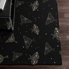 a black area rug with butterflies and stars in the night sky, on top of a wooden floor