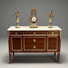 an ornately decorated sideboard with two clocks on it's top, and three smaller vases in the middle