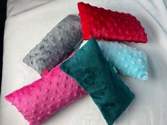 four different colored pillows laying on top of a white bed sheet, one is red, one is green and the other is blue